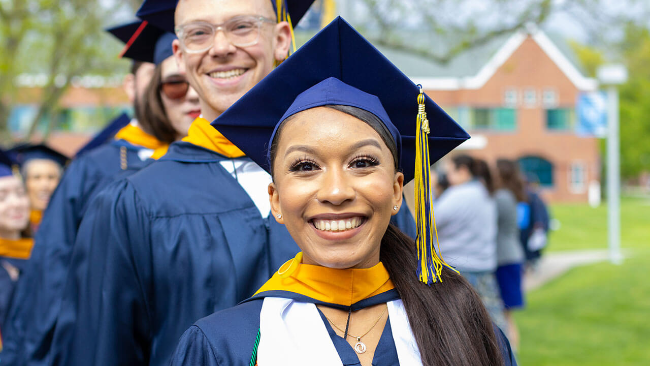 A graduate wearing a white stole smiles excitedly