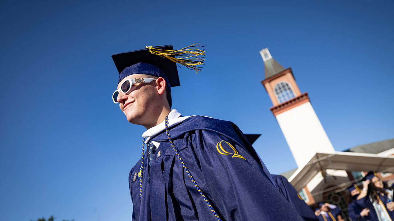 A graduate walks in front of the Arnold Bernhard Library