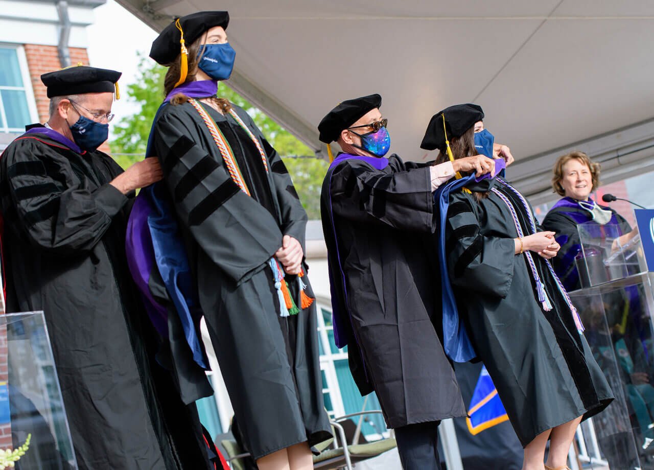 Faculty members drape doctoral hoods on two new graduates