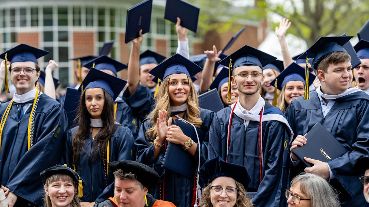 Graduates stand in rows, cheering at the end of the ceremony