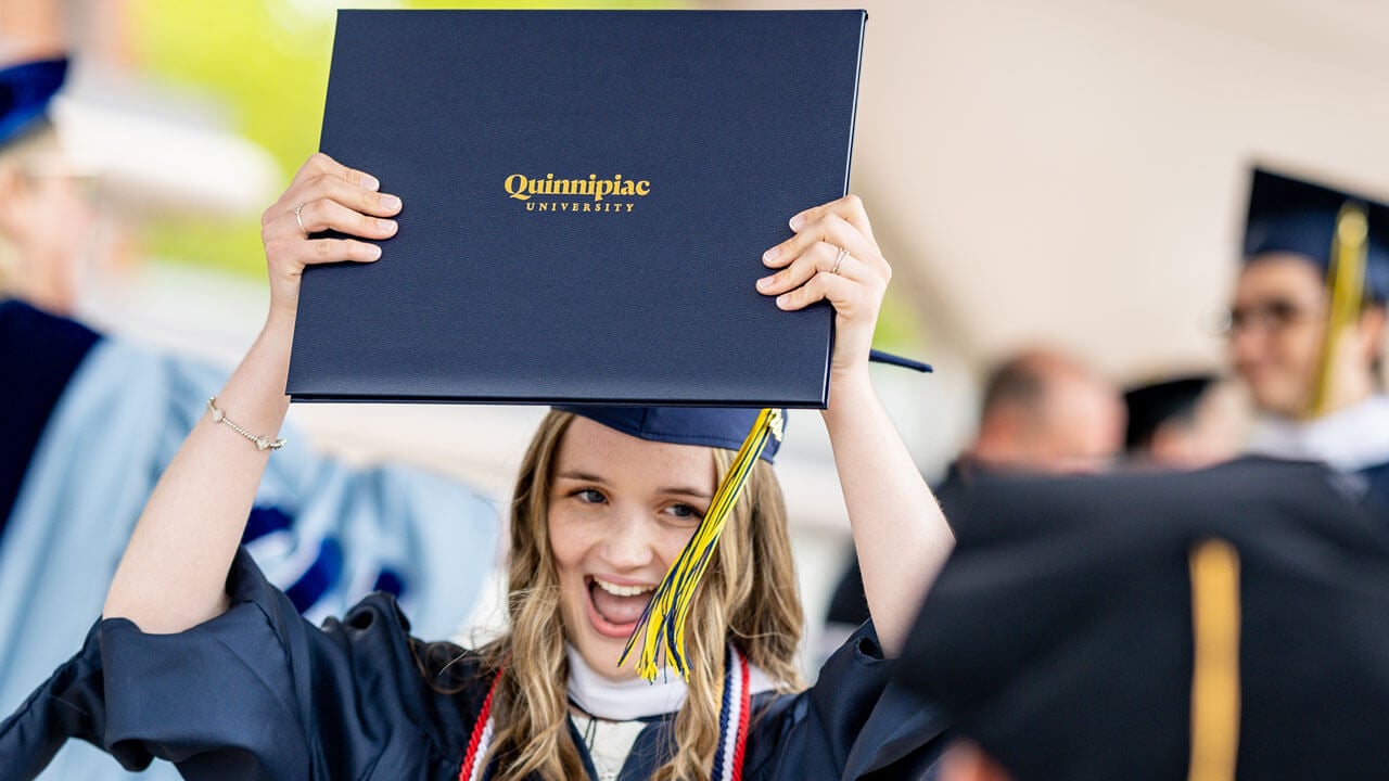 SOC graduate holds their degree in the air smiling