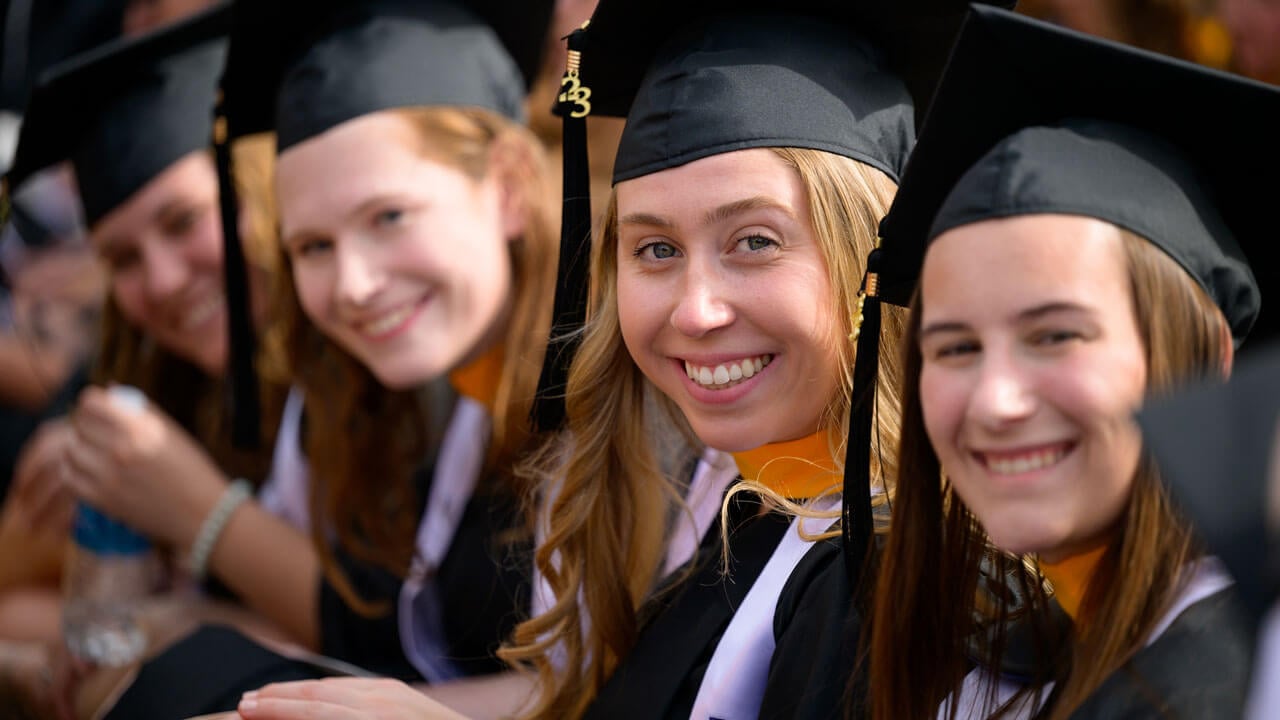 Graduates grinning while sitting in a row waiting for commencement