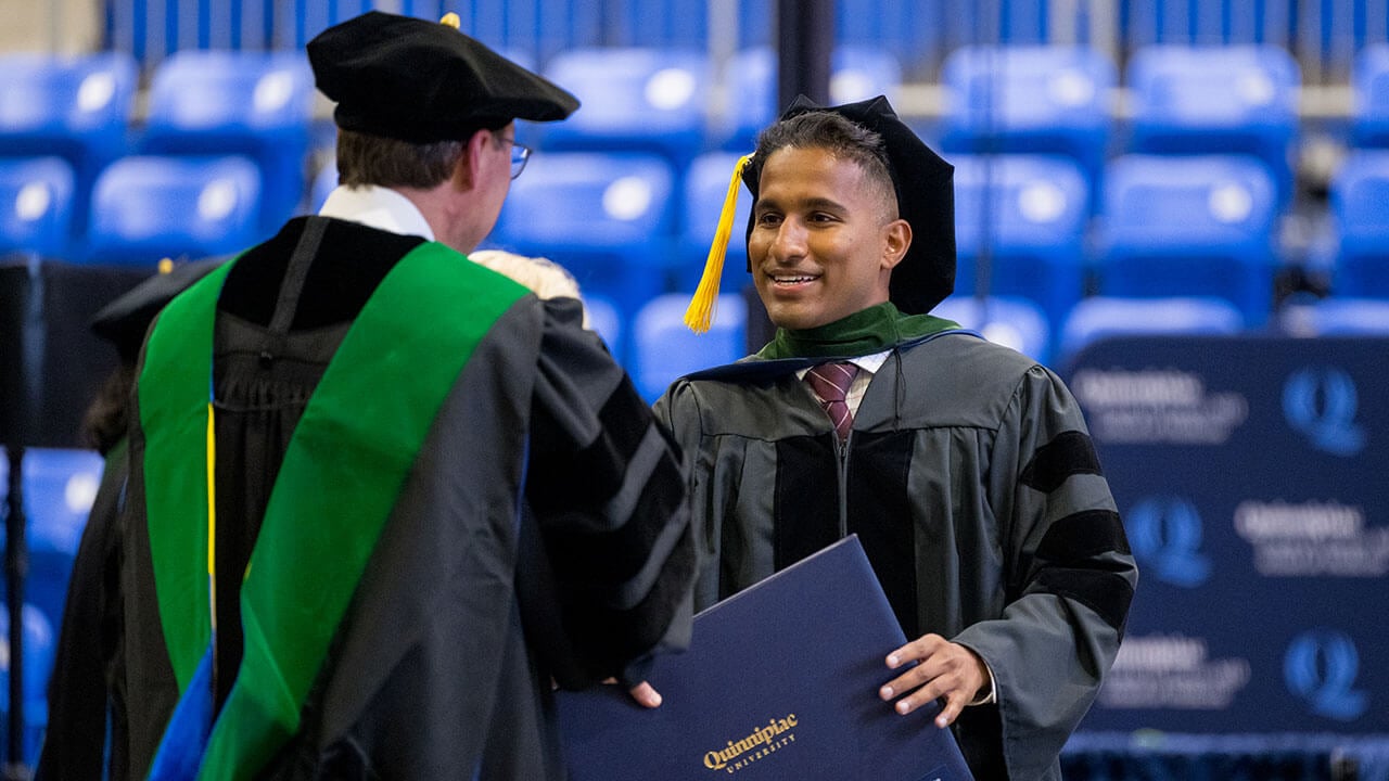 male graduate holds up his degree and smiles broadly