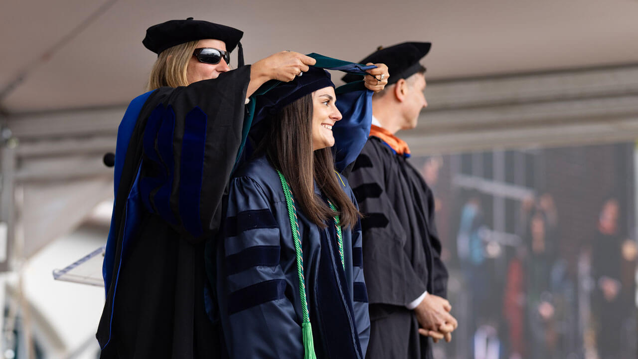 A beaming Health Sciences graduate gets hooded at the 2024 Commencement ceremony.