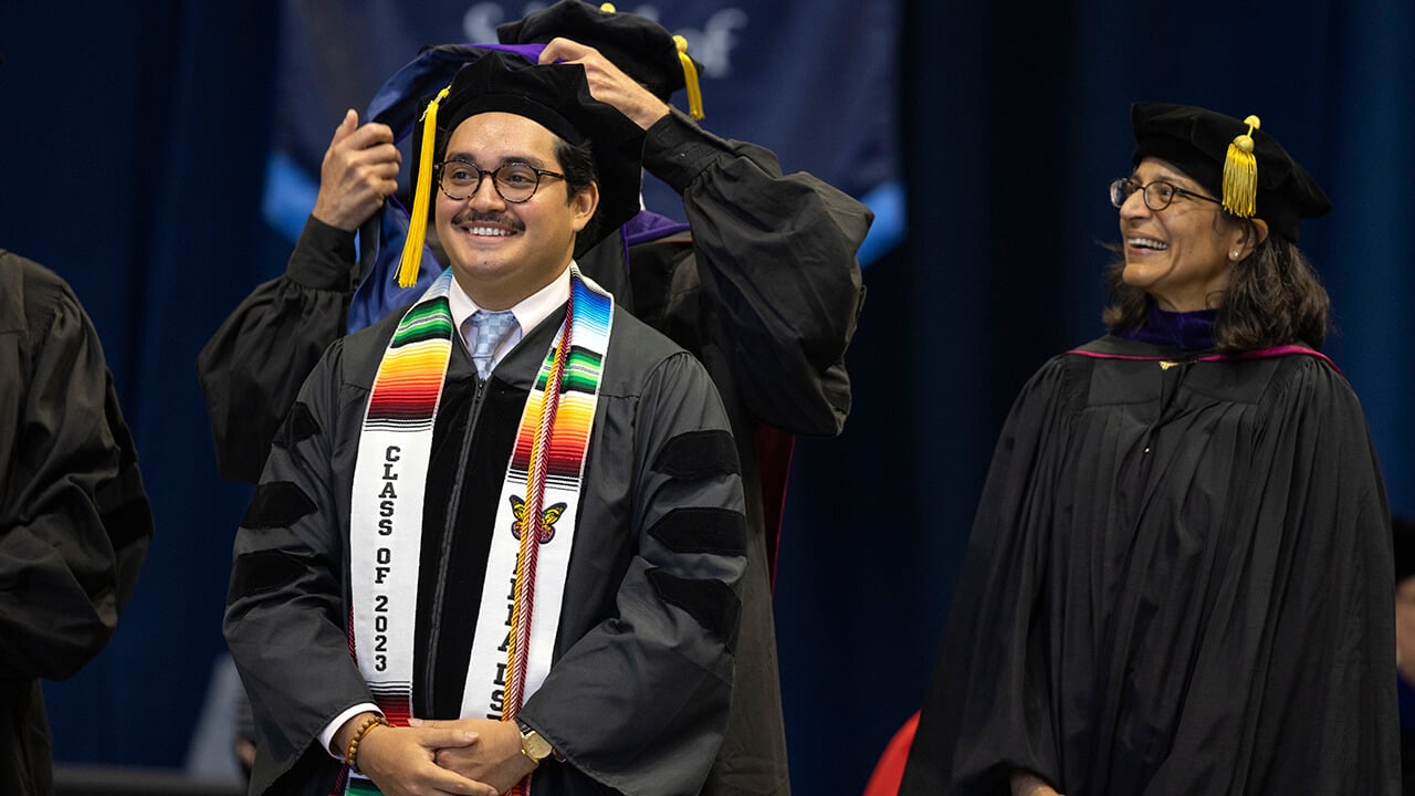 Graduate smiles as they receive their hood