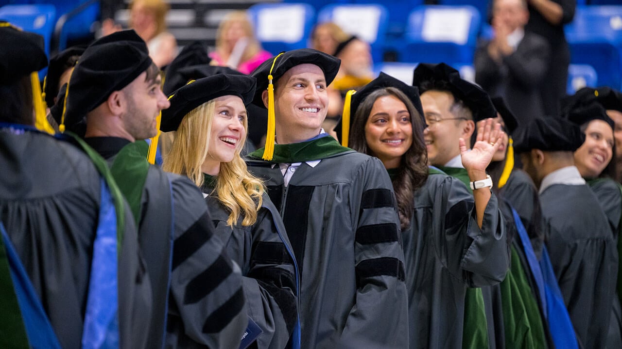 graduates turn to smile and wave at their audience