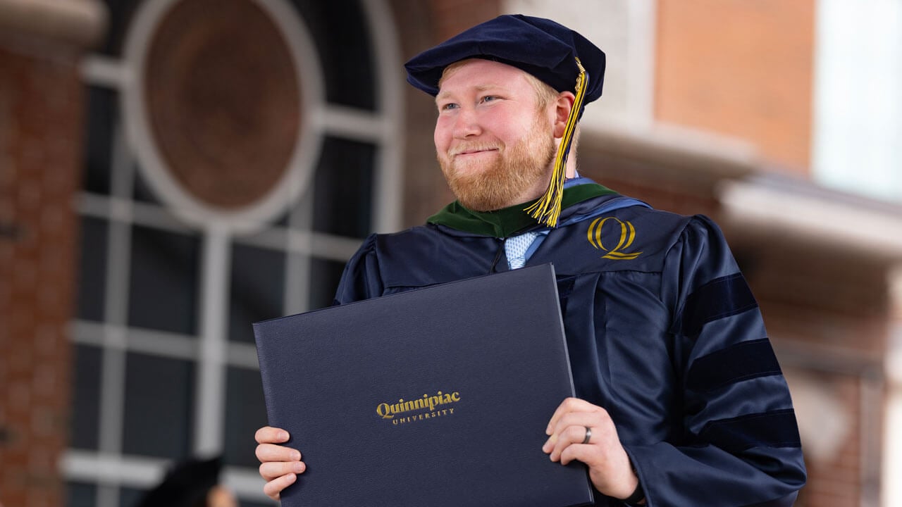 Proudly, a Health Sciences graduate holds up their diploma.