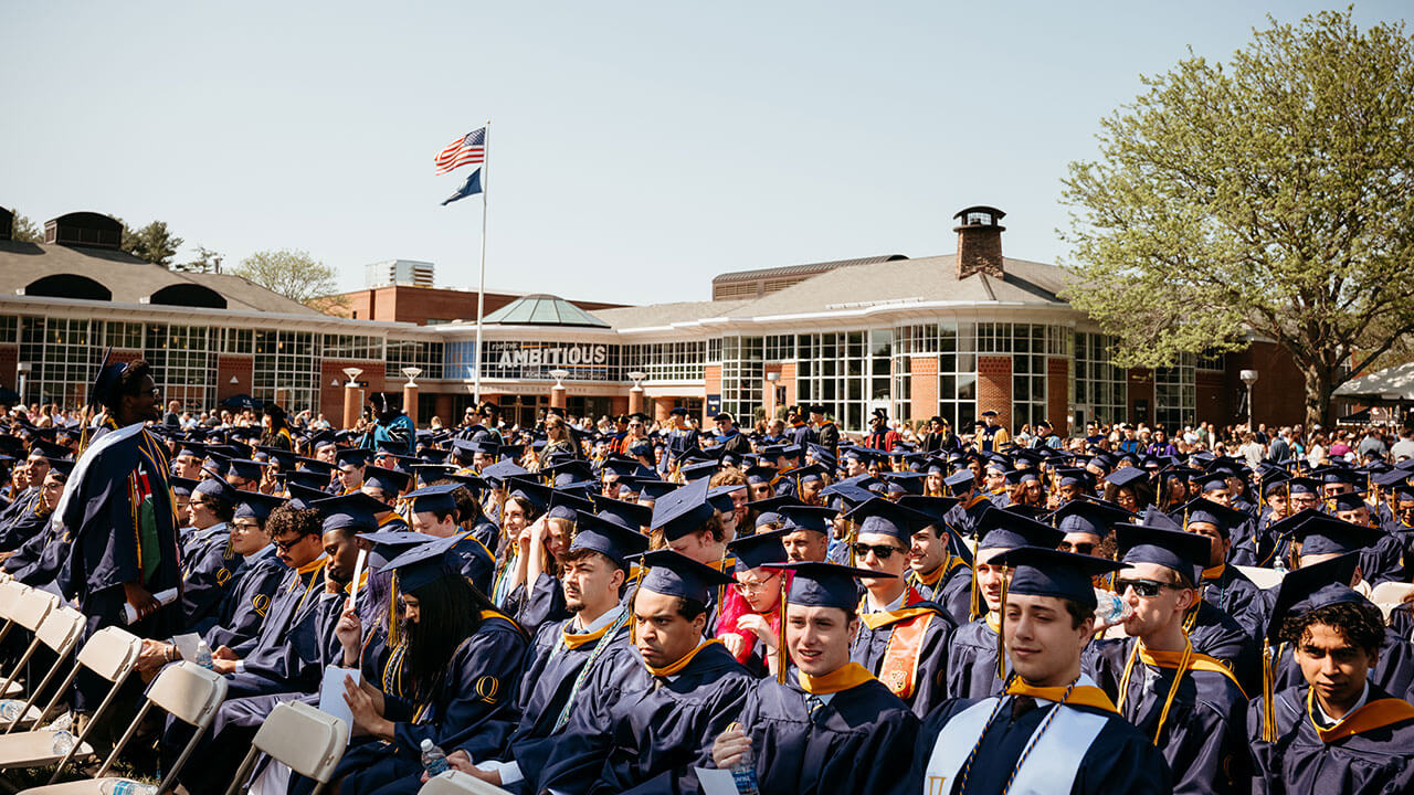 A wide angle photo of graduates sitting in their chairs on the quad.