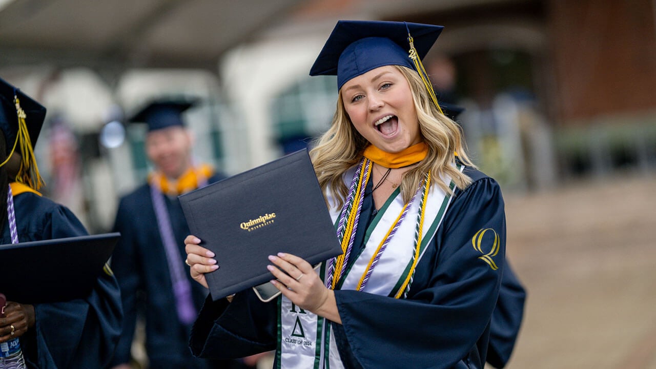 graduate smiles and poses with diploma