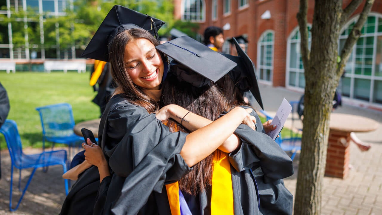 Two graduates hug with big smiles on their faces