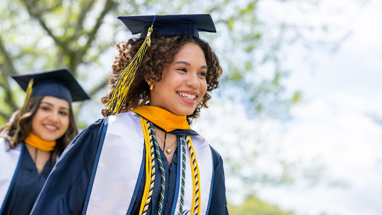 Smiling excitedly, a 2024 School of Nursing graduate eagerly walks across the quad as the Commencement ceremony begins.