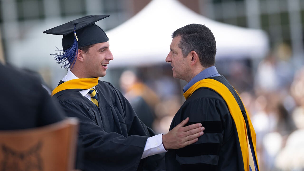 Student talking with professor in cap and gown