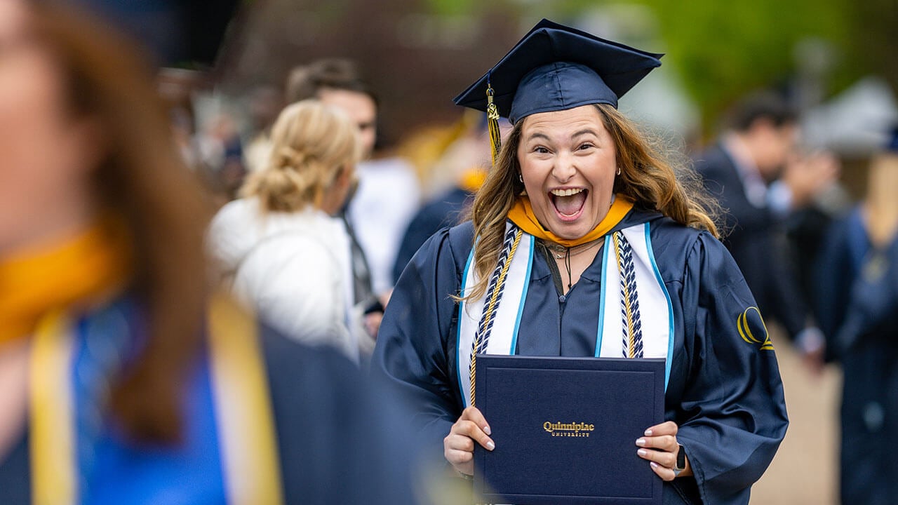 graduate smiles excitedly with diploma