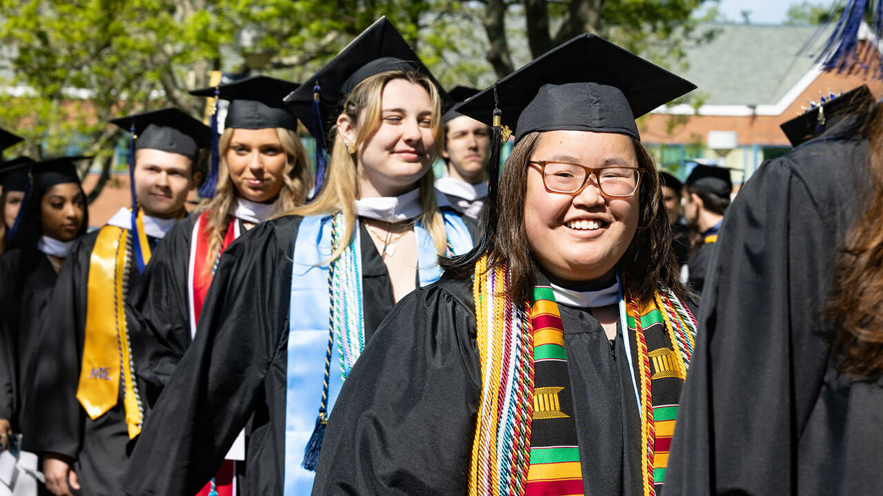 line of graduates smile at the camera and their families crowded around