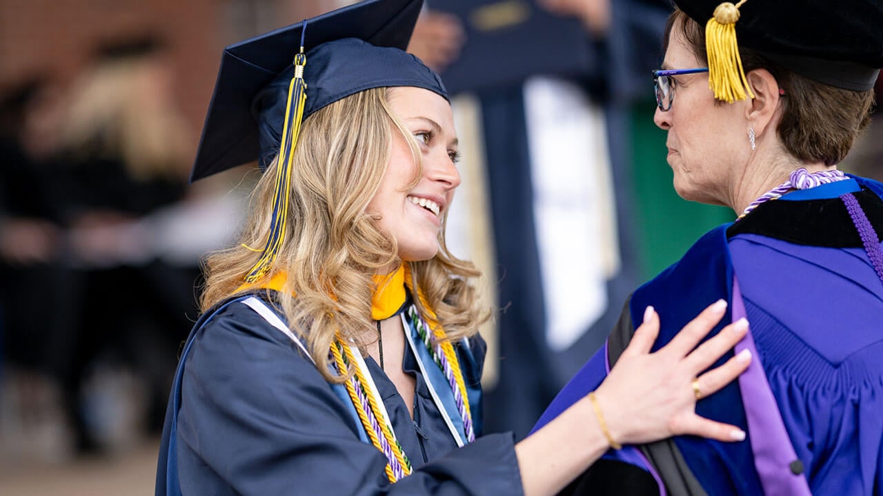 graduate hugs professor and smiles