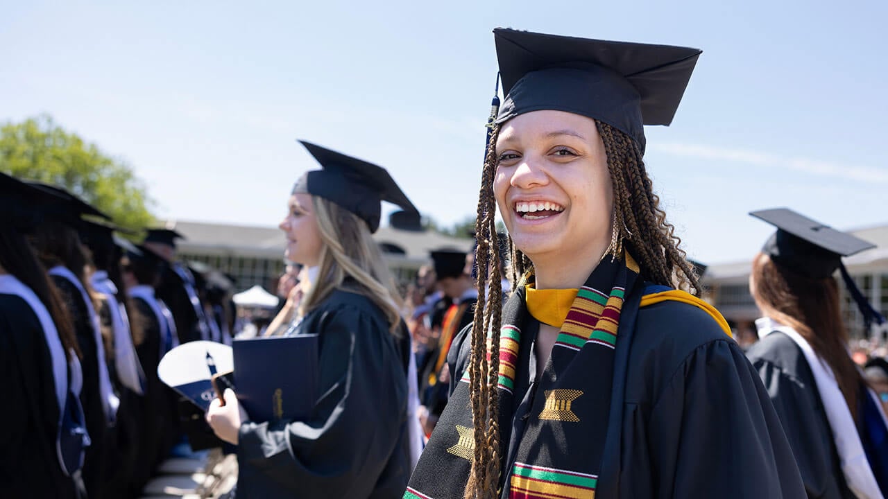 female graduate looks at the camera and laughs while sitting in her row