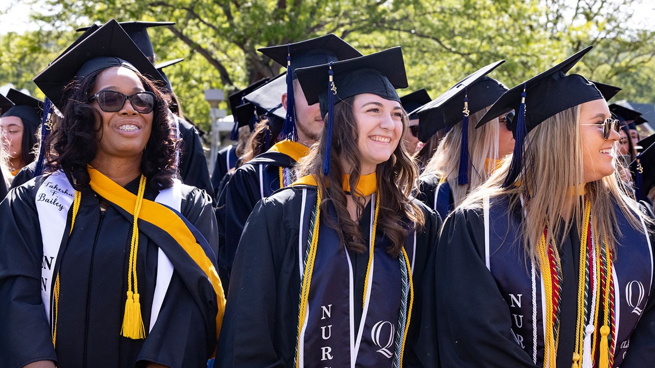 graduates smile and laugh at the crowd as they process