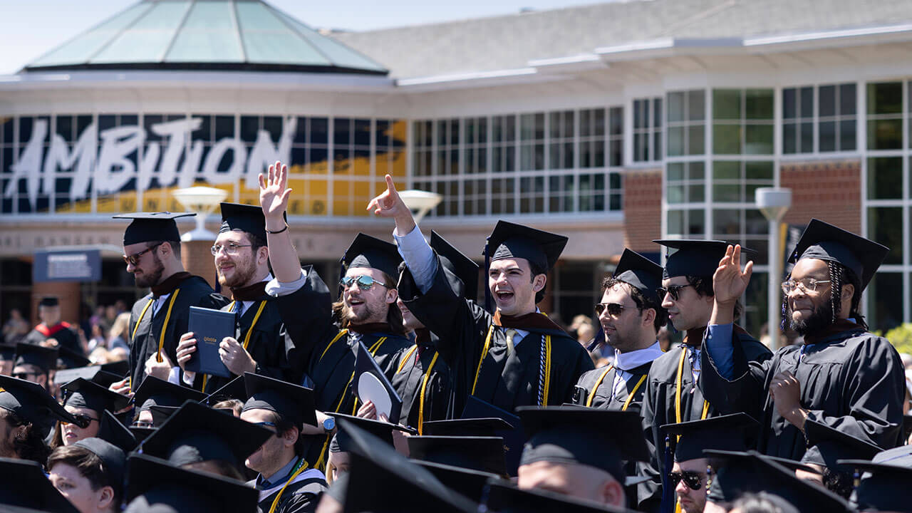 row of male graduates cheer and point out to the audience