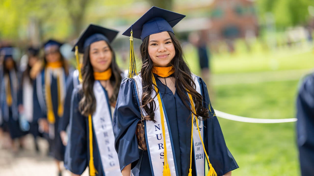 Class of 2024 School of Nursing graduate walks down the quad with their peers as they prepare to take their seats.