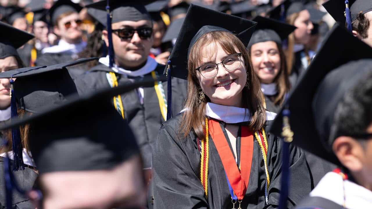 A graduate tilts her head and smiles in a sea of graduates