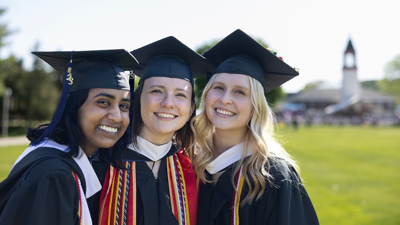 3 Graduates pose on the Quadrangle in caps and gowns