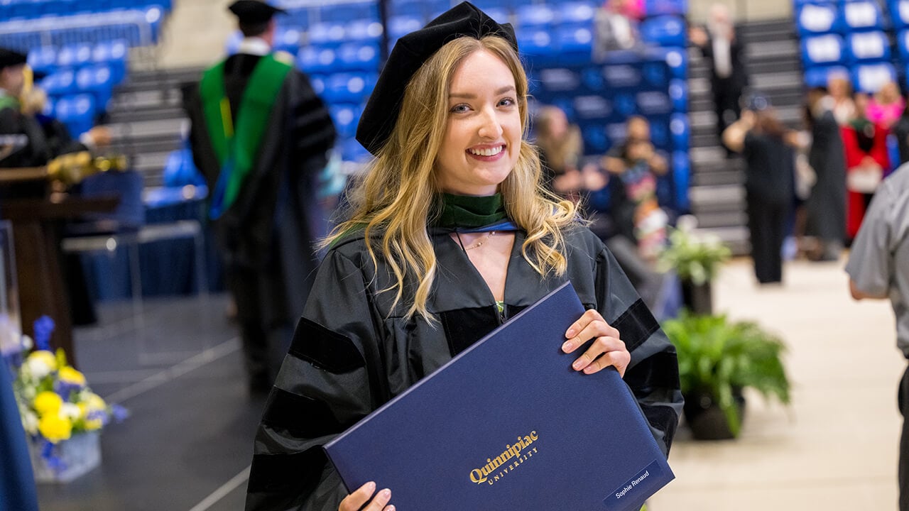 Graduate poses with diploma and smiles