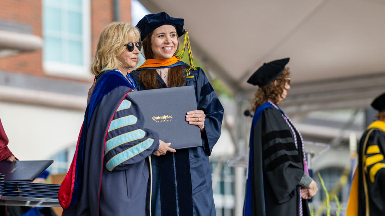 A 2024 graduate stands with President Judy Olian for a picture before taking her diploma.