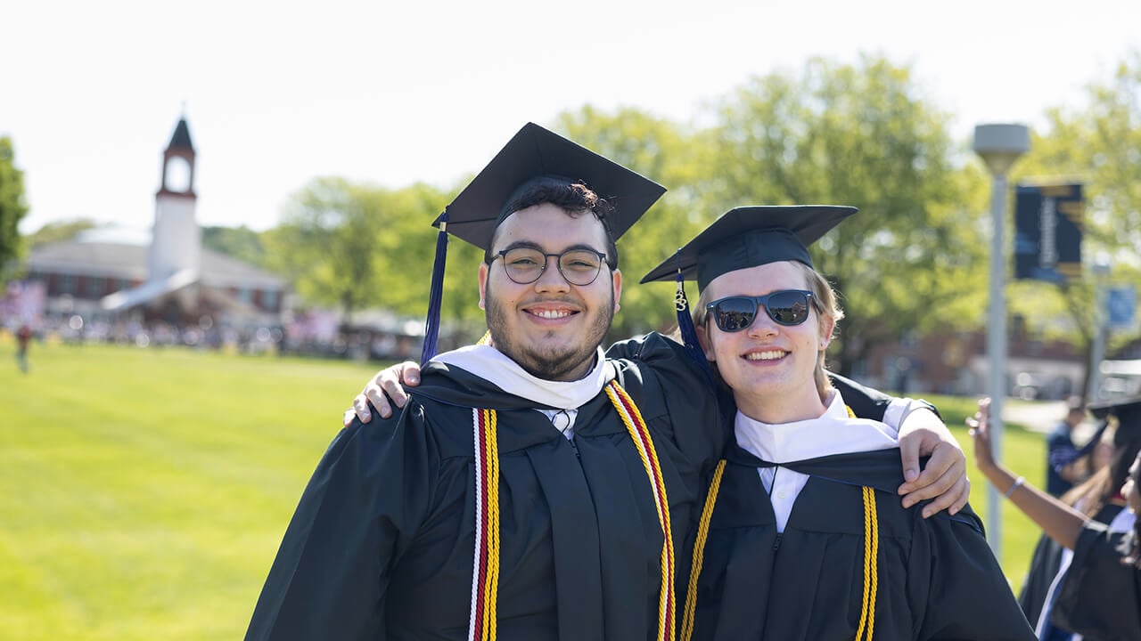 Graduates embrace and smile in front of the graduation set up on the Quadrangle