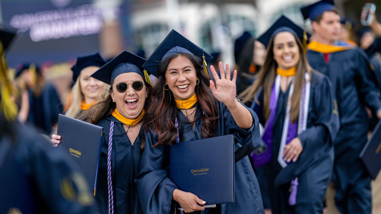 Quinnipiac graduates wave at the camera and smile