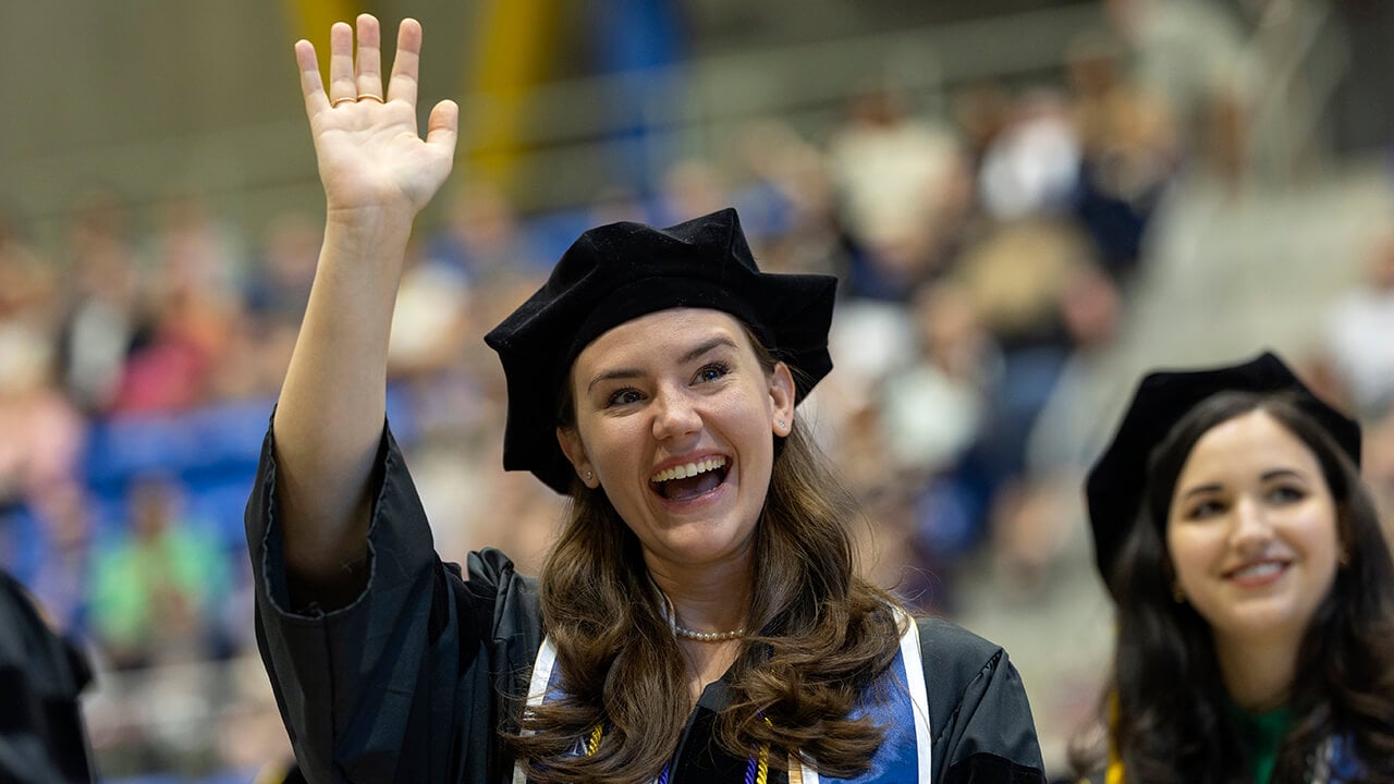 Graduate smiles and waves to family in audience