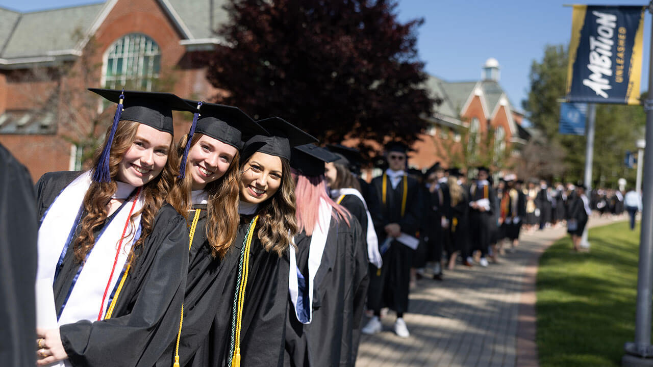 three female graduates lean out of their line and smile towards the camera