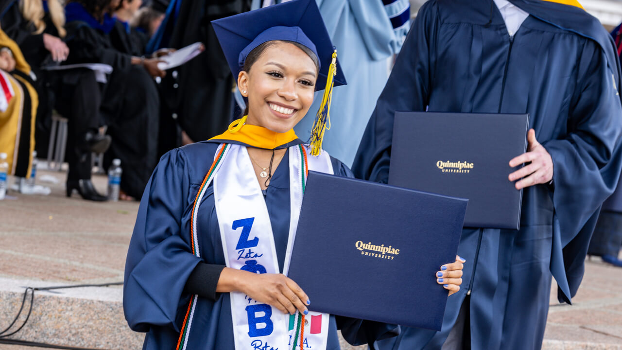 A graduate holds up her diploma and poses at the bottom of the library steps