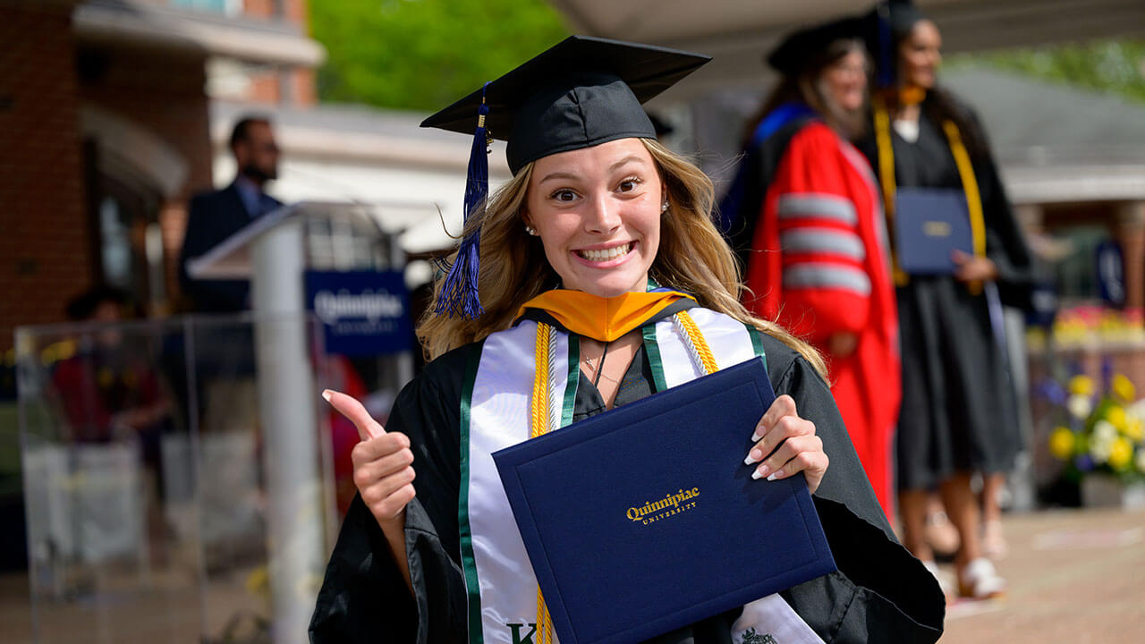 graduate flashes the camera a thumbs up with a big grin and her diploma