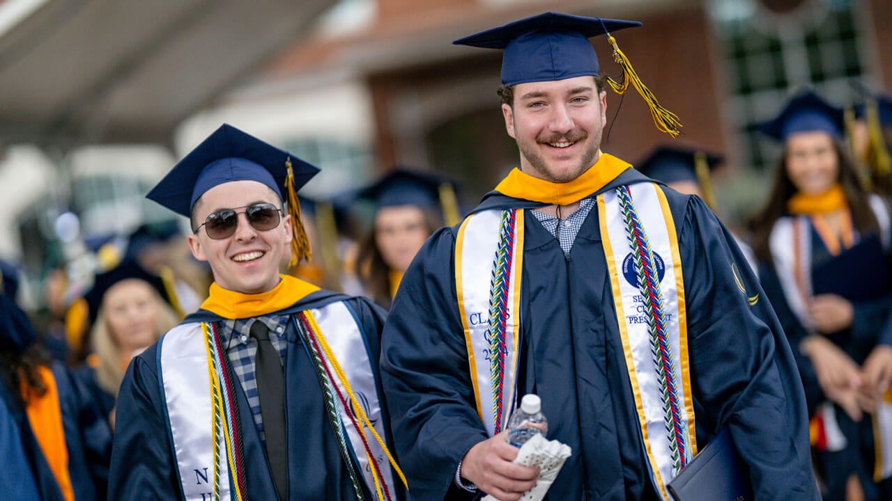 Two 2024 Nursing graduates smile brightly as they walk back to their seats after receiving their diplomas.