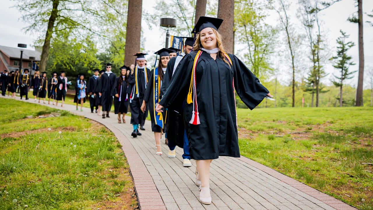 Graduate smiles as she leads a group of graduates to the Quad