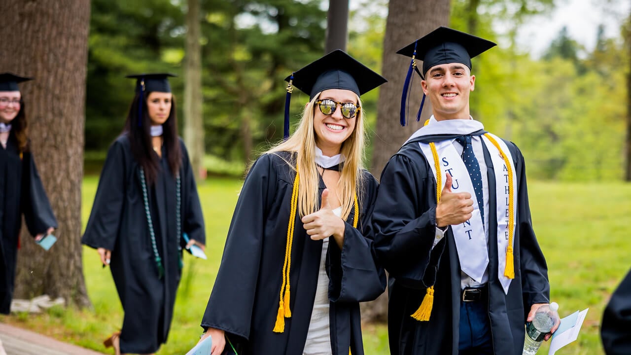 Two graduates give a thumbs up by the College of Arts and Sciences