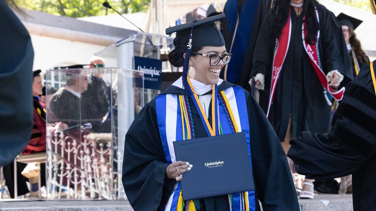 A graduate holds up her diploma cover and smiles