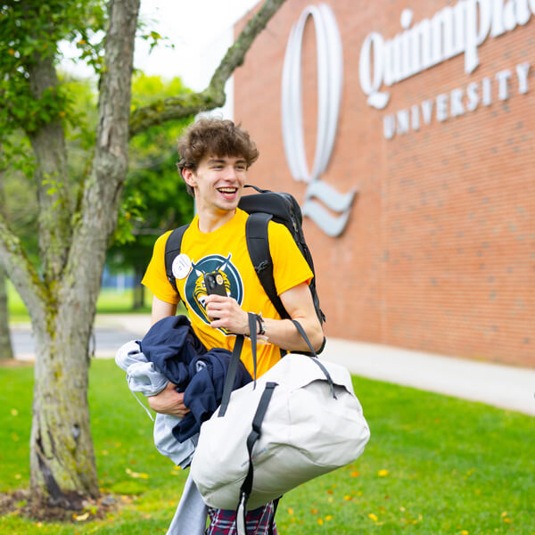 A new student carries a bag and backpack as he enters Quinnipiac Orientation
