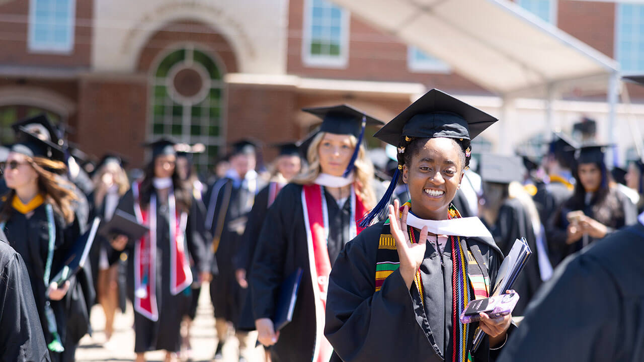 graduate smiles and waves at the camera while processing out