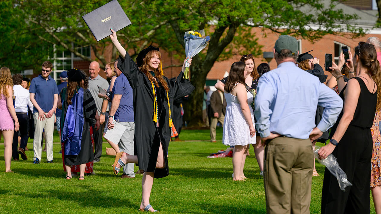 Graduate raises flowers in one hand and diploma in other on the Quadrangle