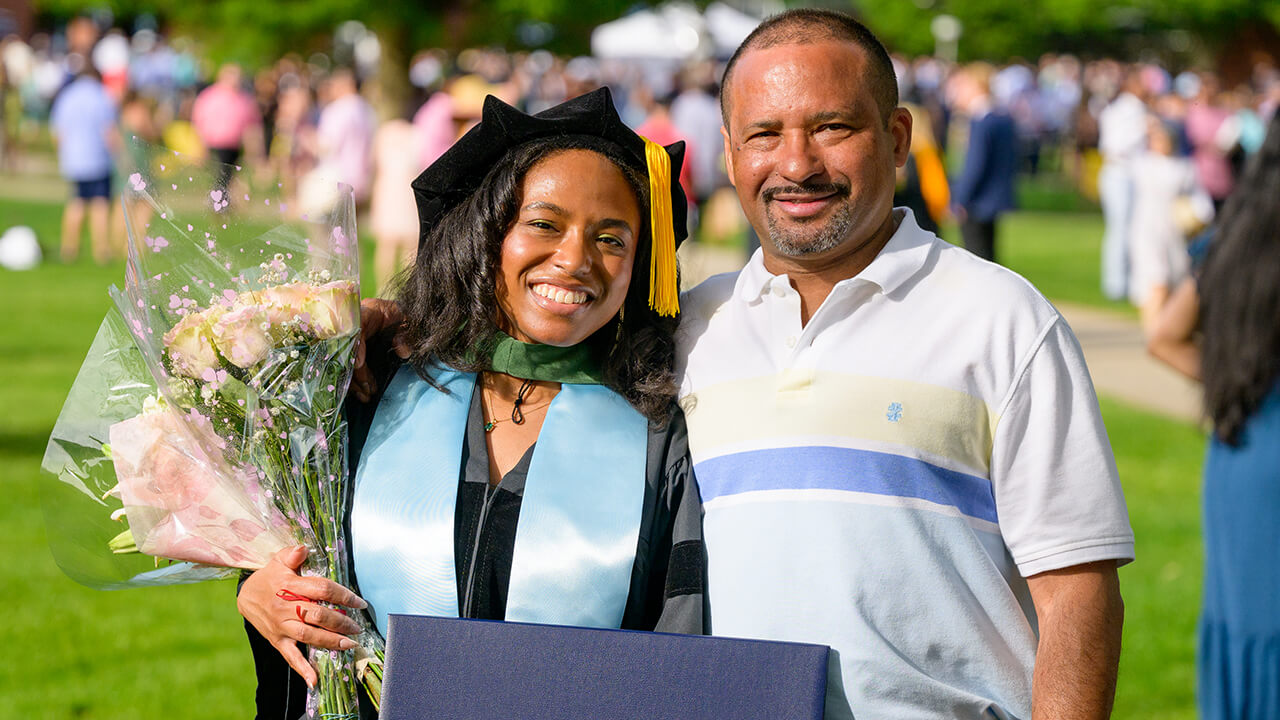 Family poses with graduate while holding flowers and diploma in a teal stole and green hood