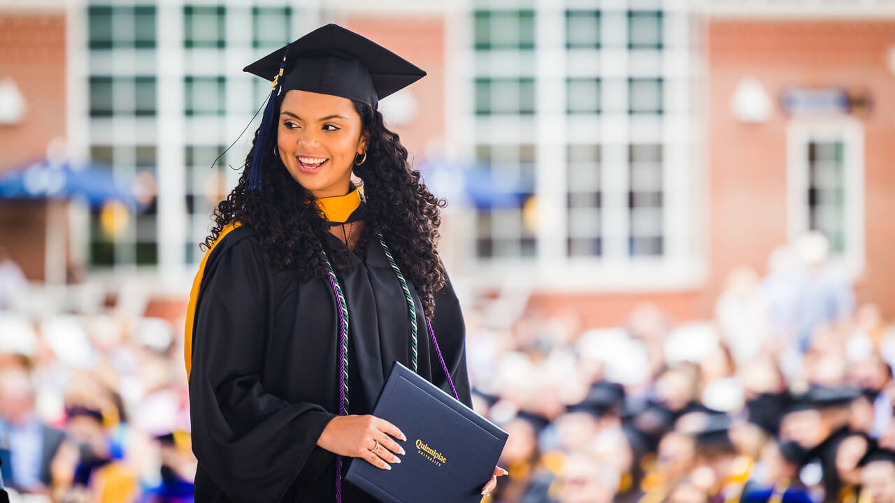 A graduate smiles with her diploma cover on stage