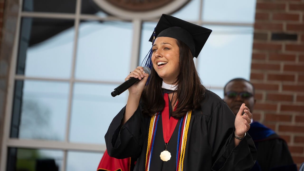 Graduate sings the National Anthem on the library steps