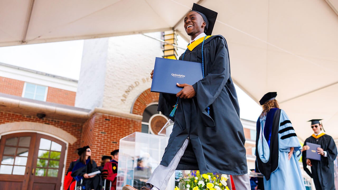 Smiling student walking across the stage with his diploma