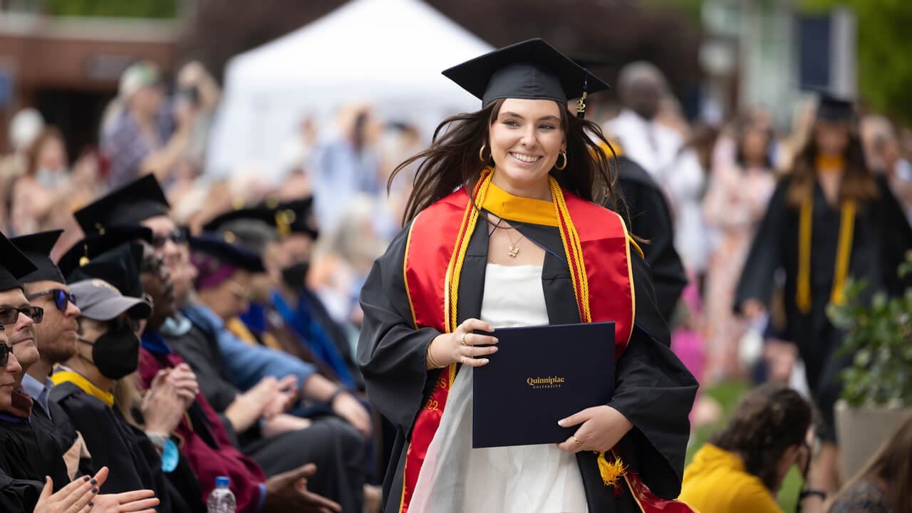 Graduate walks down the Quad with her diploma