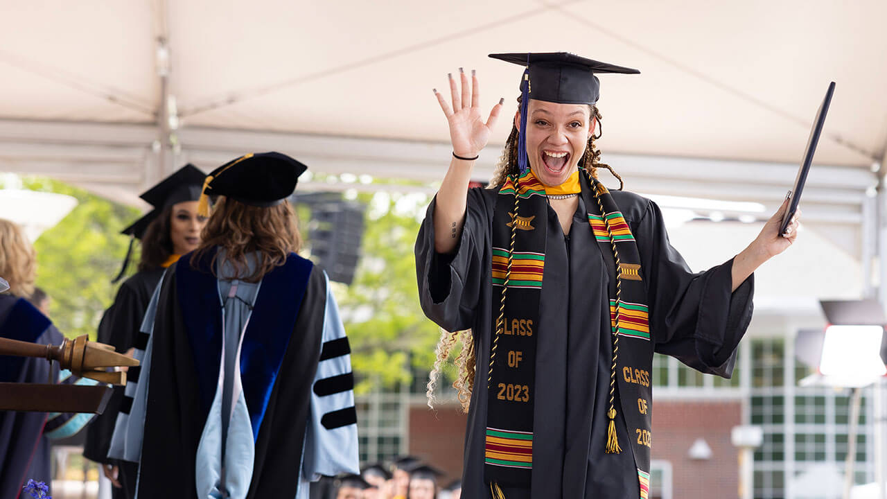 Student smiling while waving with her diploma in hand