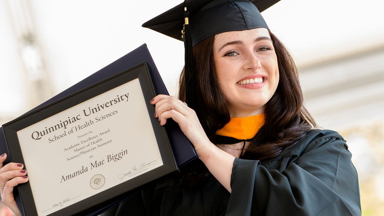 Graduate holds up their diploma and award