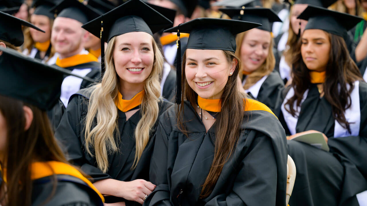 Two graduates sitting next to each other and smiling together