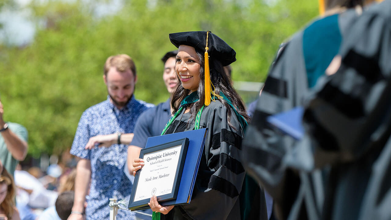 Graduate holds her diploma and smiles