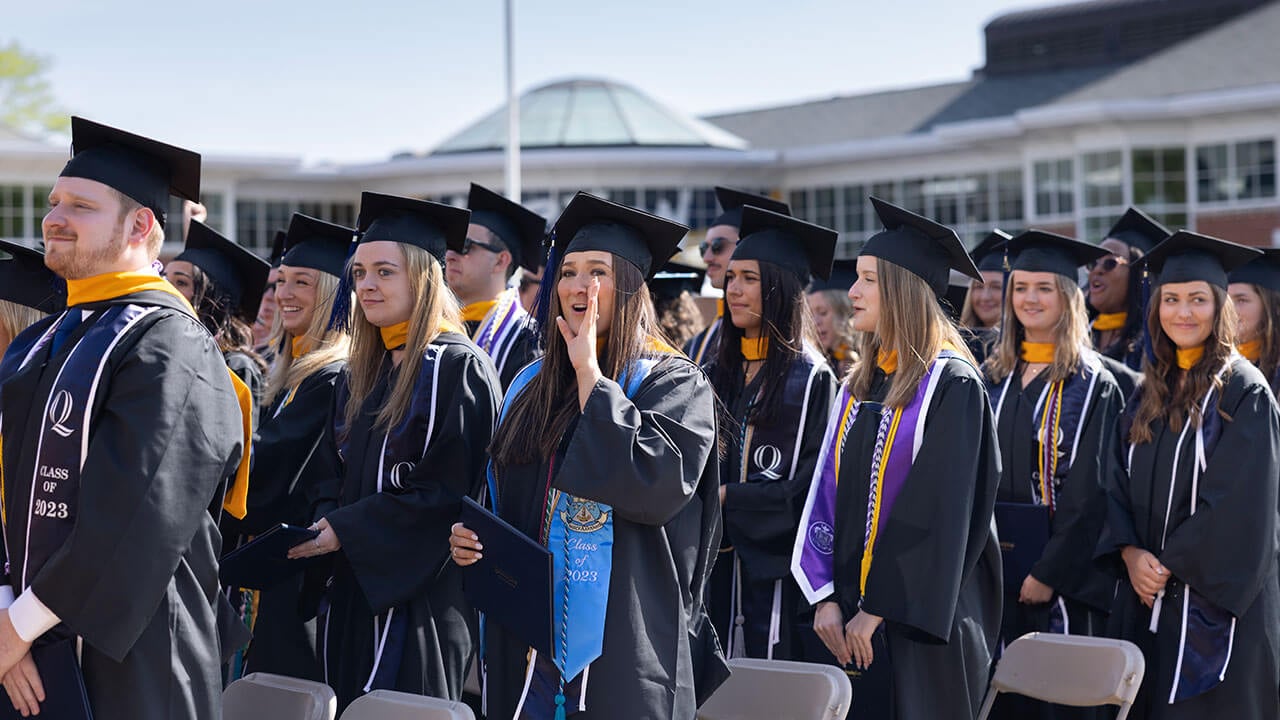 group of graduates stand in their rows smiling at the stage